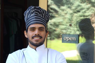 Yakışıklı Latin aşçının portresi. Üniformalı ve şapkalı. Restoran kapısının önünde.