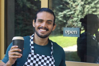 Kapının önünde kağıt kahve fincanı olan, üniformalı, yakışıklı, küçük işletme sahibinin portresi.