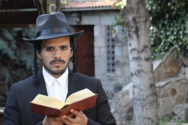 Geleneksel şapkalı yakışıklı hahamın doğal arka planda Tanakh ile yakın plan portresi.