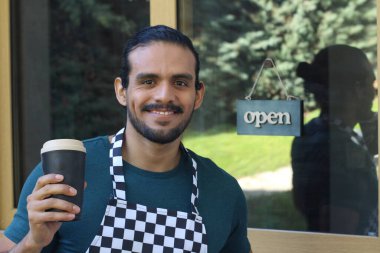 Kapının önünde kağıt kahve fincanı olan, üniformalı, yakışıklı, küçük işletme sahibinin portresi.