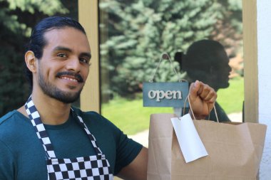 Kapının önünde kağıt torba ve açık hesap ile yakışıklı Latin üniformalı küçük işletme sahibi portresi