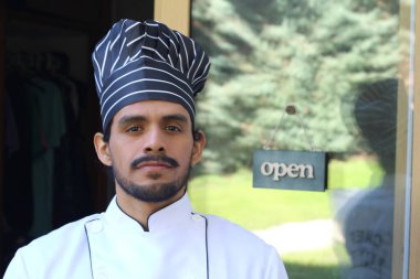 Yakışıklı Latin aşçının portresi. Üniformalı ve şapkalı. Restoran kapısının önünde.