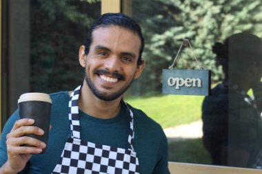 Kapının önünde kağıt kahve fincanı olan, üniformalı, yakışıklı, küçük işletme sahibinin portresi.