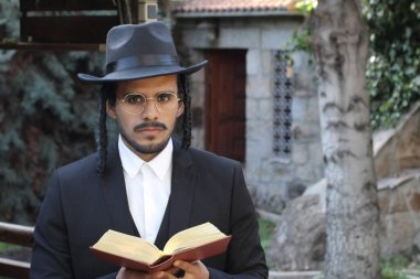 Geleneksel şapkalı yakışıklı hahamın doğal arka planda Tanakh ile yakın plan portresi.