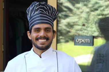 Yakışıklı Latin aşçının portresi. Üniformalı ve şapkalı. Restoran kapısının önünde.