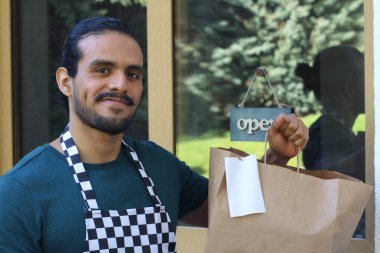 Kapının önünde kağıt kahve fincanı olan, üniformalı, yakışıklı, küçük işletme sahibinin portresi.