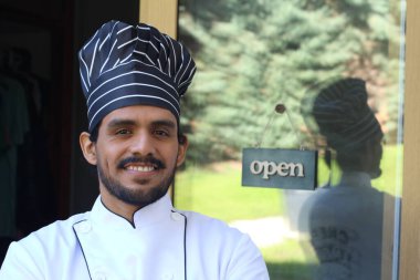 Yakışıklı Latin aşçının portresi. Üniformalı ve şapkalı. Restoran kapısının önünde.
