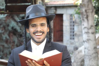 Geleneksel şapkalı yakışıklı hahamın doğal arka planda Tanakh ile yakın plan portresi.