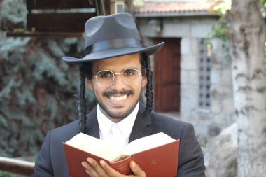 Geleneksel şapkalı yakışıklı hahamın doğal arka planda Tanakh ile yakın plan portresi.
