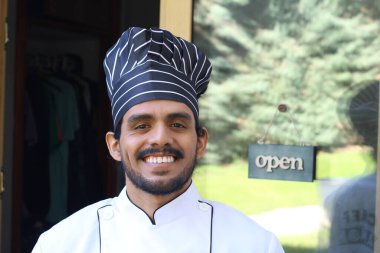 Yakışıklı Latin aşçının portresi. Üniformalı ve şapkalı. Restoran kapısının önünde.