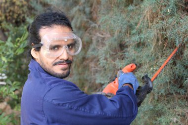 Çalıları kesen elektrikli testereli yakışıklı bahçıvanın yakın plan portresi.