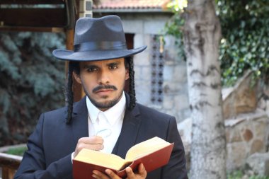 Geleneksel şapkalı yakışıklı hahamın doğal arka planda Tanakh ile yakın plan portresi.