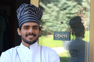 Yakışıklı Latin aşçının portresi. Üniformalı ve şapkalı. Restoran kapısının önünde.