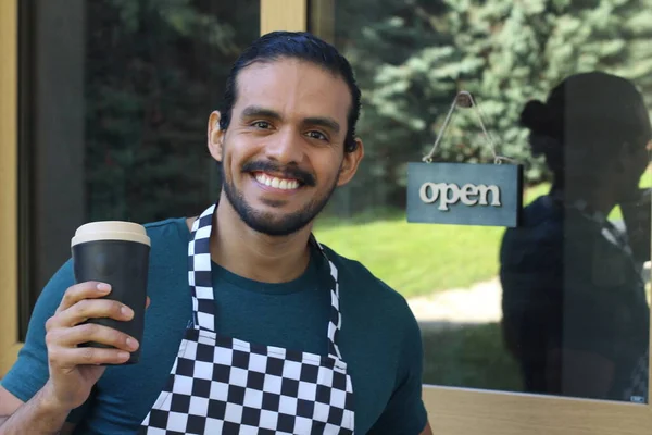 Kapının önünde kağıt kahve fincanı olan, üniformalı, yakışıklı, küçük işletme sahibinin portresi.