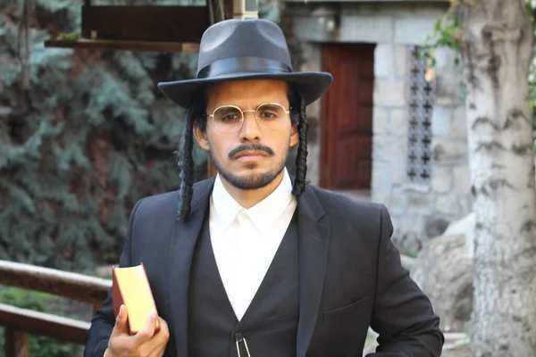 Geleneksel şapkalı yakışıklı hahamın doğal arka planda Tanakh ile yakın plan portresi.