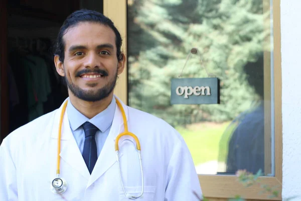 portrait of handsome young Latin doctor with stethoscope in front of his office door with open tab