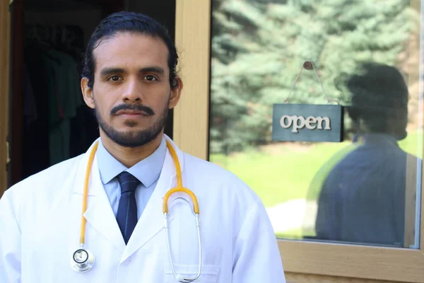 portrait of handsome young Latin doctor with stethoscope in front of his office door with open tab