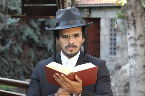 Geleneksel şapkalı yakışıklı hahamın doğal arka planda Tanakh ile yakın plan portresi.