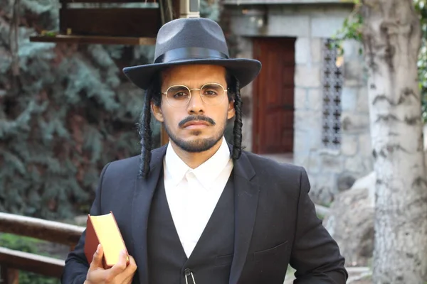 Geleneksel şapkalı yakışıklı hahamın doğal arka planda Tanakh ile yakın plan portresi.