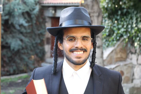 Geleneksel şapkalı yakışıklı hahamın doğal arka planda Tanakh ile yakın plan portresi.