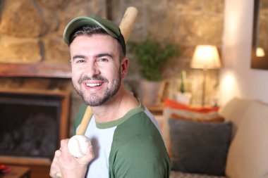 Evde beyzbol sopası ve topu olan yakışıklı bir gencin portresi.