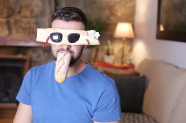 Ekmek gözlüklü yakışıklı genç bir adam. Ağzında baget var.