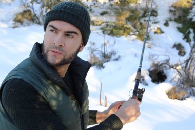 Kışın ormanda elinde olta tutan kalın elbiseli yakışıklı bir genç.
