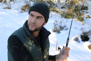 Kışın ormanda elinde olta tutan kalın elbiseli yakışıklı bir genç.