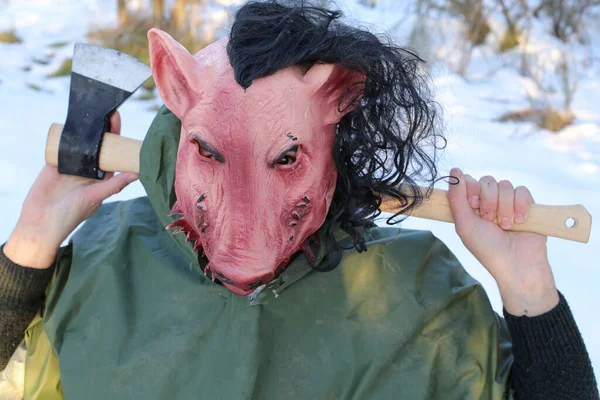 man in horror pig mask holding axe in winter forest