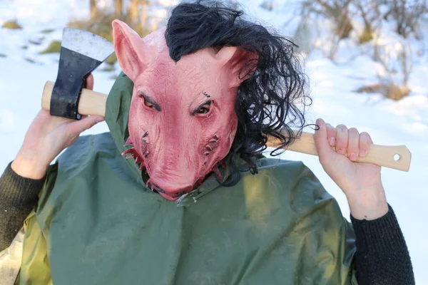 man in horror pig mask holding axe in winter forest