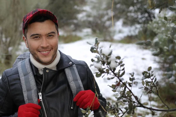 handsome young man in leather jacket with backpack in winter forest