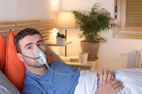 handsome young man with medical oxygen mask in bed at home