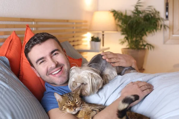 ハンサムな若い男と犬猫は家でベッドでリラックスして — ストック写真