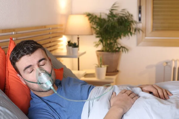 handsome young man with medical oxygen mask in bed at home