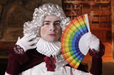 Viktorya tarzı kostümlü genç adam elinde lgbtq renkli yelpaze tutuyor.