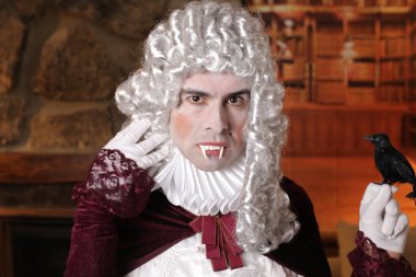 Vampir dişli Viktorya tarzı kostümlü genç adam içeride poz veriyor.