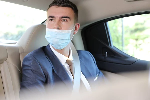 close-up portrait of handsome young businessman in medical mask on back seat of car