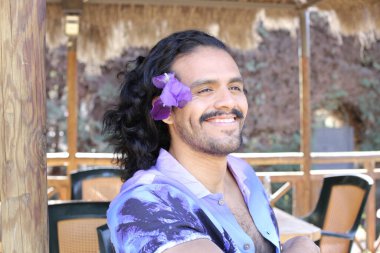 Açık havada orkide çiçekli, şık, mor gömlekli genç bir adamın portresi.