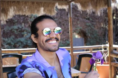 Açık havada orkide çiçekli, şık, mor gömlekli genç bir adamın portresi.