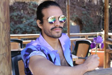 Açık havada orkide çiçekli, şık, mor gömlekli genç bir adamın portresi.