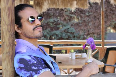 Açık havada orkide çiçekli, şık, mor gömlekli genç bir adamın portresi.