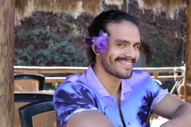 Açık havada orkide çiçekli, şık, mor gömlekli genç bir adamın portresi.