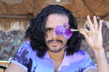 Açık havada orkide çiçekli, şık, mor gömlekli genç bir adamın portresi.