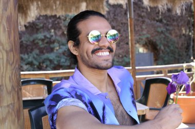 Açık havada orkide çiçekli, şık, mor gömlekli genç bir adamın portresi.