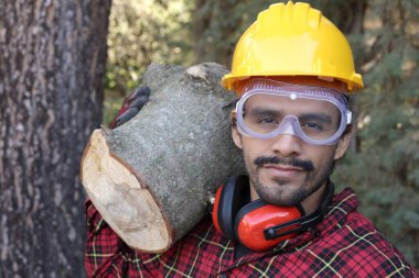 Kasklı yakışıklı oduncunun portresi omuzunda kütük tutuyor.