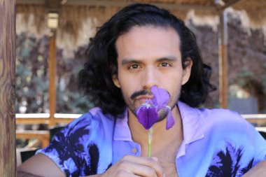 Açık havada orkide çiçekli, şık, mor gömlekli genç bir adamın portresi.