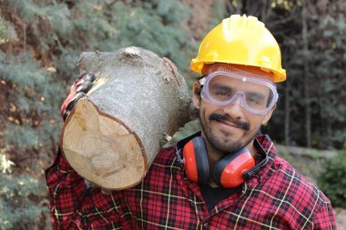 Kasklı yakışıklı oduncunun portresi omuzunda kütük tutuyor.