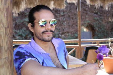 Açık havada orkide çiçekli, şık, mor gömlekli genç bir adamın portresi.