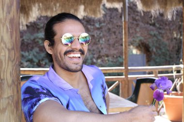 Açık havada orkide çiçekli, şık, mor gömlekli genç bir adamın portresi.