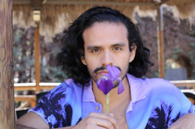 Açık havada orkide çiçekli, şık, mor gömlekli genç bir adamın portresi.